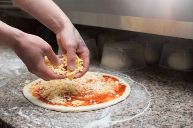 Mutfaktaki genç adam pizzaya malzeme koyar. Yakın plan. Pizza teslimatı.