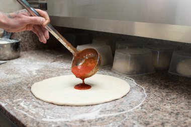 Erkek aşçı pizzanın üzerine acı sos döker. Çiğ hamur preformu. Pizza üretimi ve teslimatı.