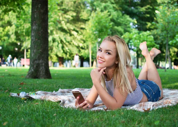 在一个阳光明媚的夏日 一个非常漂亮的金发姑娘正躺在草地上 一边打电话一边自言自语 — 图库照片