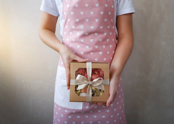 Hands of a young woman holding a gift with sweets. Closeup of a box of handmade candies in hands. Sweet Valentine\'s Day Gift. International Women\'s Day.