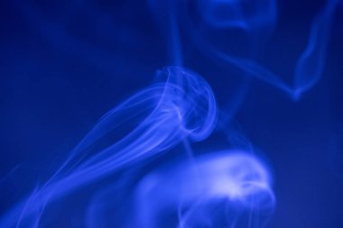 Koyu arkaplanda mavi ışıkta dönen duman bulutları.