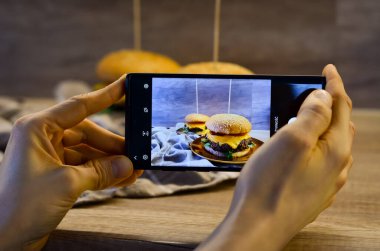 Bir adam tabakta ev yapımı hamburgerlerin fotoğrafını çekiyor.