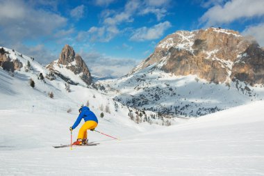Male skier in blue and yellow clothes on slope with mountains in the background at Cortina d'Ampezzo Col Gallina Sella Ronda skiing resort area Dolomiti Italy clipart