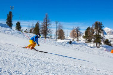 Dolomiti İtalya kayak merkezi Cortina d 'Ampezzo Faloria' nın arka planında dağlarla birlikte yamaçta mavi ve sarı elbiseli erkek kayakçı.