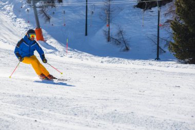 Dolomiti İtalya kayak merkezi Cortina d 'Ampezzo Faloria' nın arka planında dağlarla birlikte yamaçta mavi ve sarı elbiseli erkek kayakçı.
