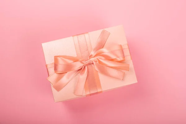 バレンタインデーギフトボックスにストライプ紙で包まれ テキストのためのコピースペースとピンクの背景にシルクリボン弓で結ばれています — ストック写真