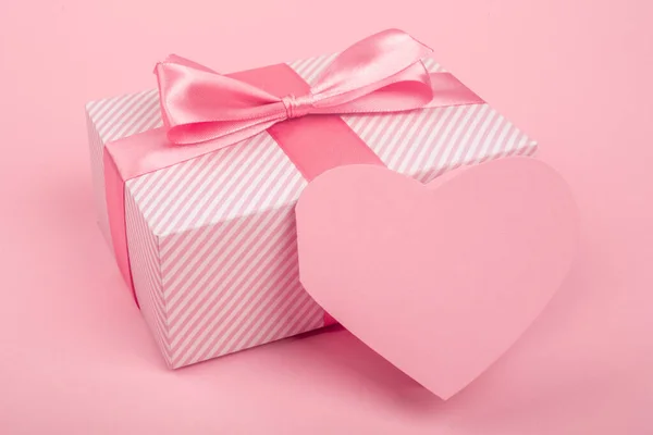 情人节礼物装在一个盒子里 盒子里用条纹纸包着 用丝带 蝴蝶结和心形贺卡捆着 粉红的背景上有文字的复制空间 — 图库照片
