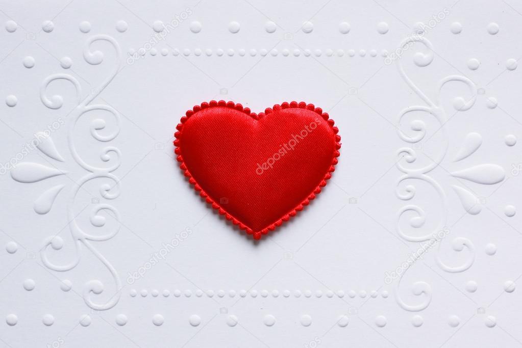 Blank embossed white paper with red satin hearts on it.