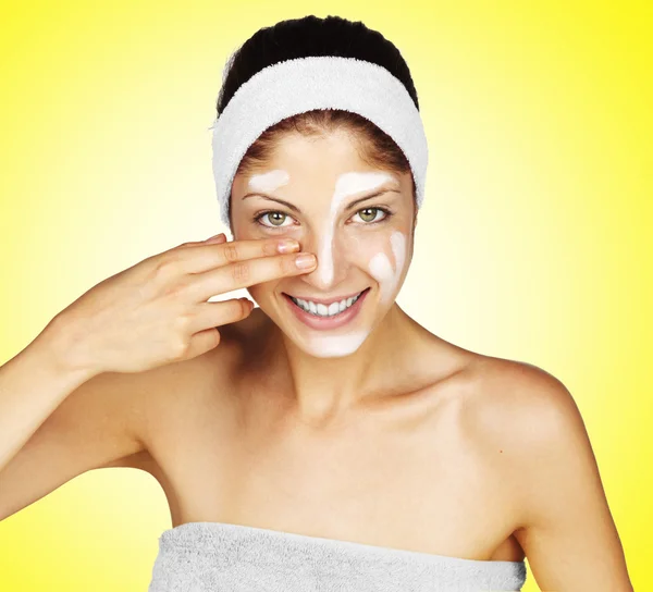 Krásná mladá žena použití crème na tváři - na žlutém podkladu — Stock fotografie