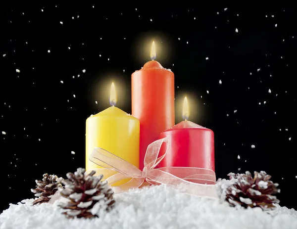 Three christmas candles and pine cones in a snow background. — Stock Photo, Image