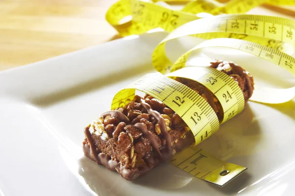 Barra de muesli de chocolate com fita métrica em um prato — Fotografia de Stock