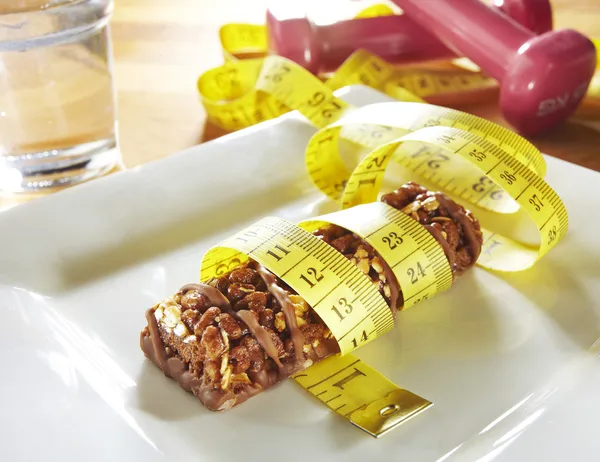 Barra de muesli de chocolate com fita métrica e pesos — Fotografia de Stock