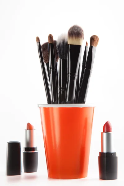Cosmetic brushes in orange cup and lipsticks — Stock Photo, Image