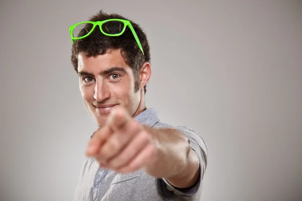 Portraiit of a young man pointing with his finger against a grey background — Stock Photo, Image