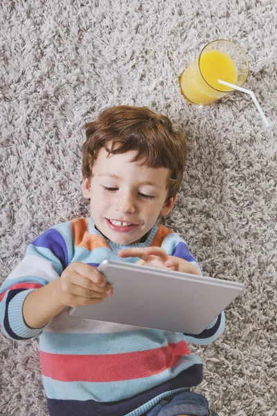 Niño jugando con la tableta digital estirada en una alfombra —  Fotos de Stock
