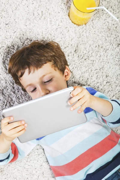 Niño jugando con la tableta digital estirada en una alfombra —  Fotos de Stock