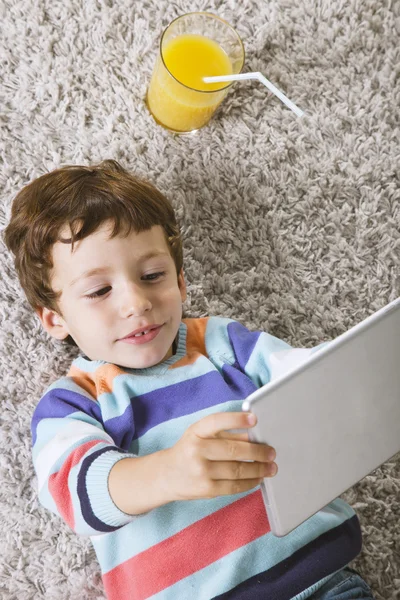 Дитина грає з цифровим планшетом, розтягнутим на килимі — стокове фото