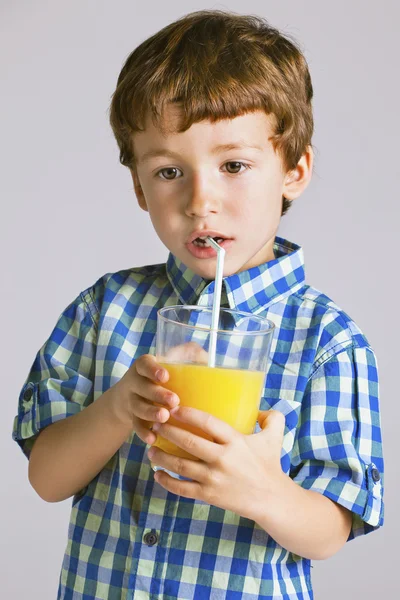 Criança com camisa xadrez bebendo um suco de laranja fresco . — Fotografia de Stock