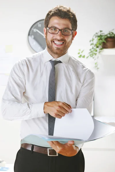 Joven hombre de negocios sonriendo y sujeto algunos papeles en la oficina . — Foto de Stock