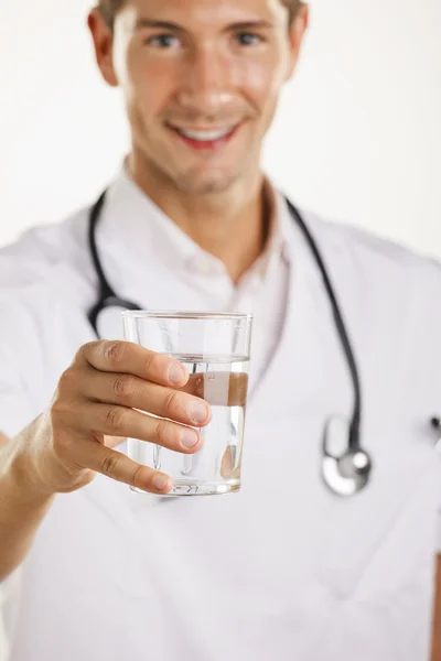 Joven médico hombre con estetoscopio mostrando un vaso de agua . — Foto de Stock