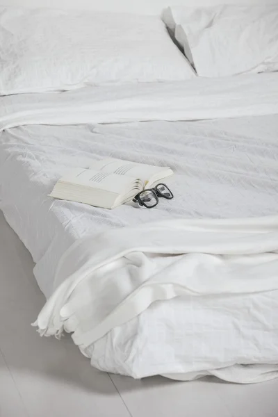 The white bedroom. Closeup of old book and rimmed glasses on bed. — Stock Photo, Image