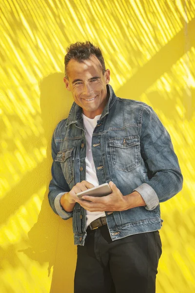 Hombre mayor tocando la tableta digital en una pared amarilla . — Foto de Stock