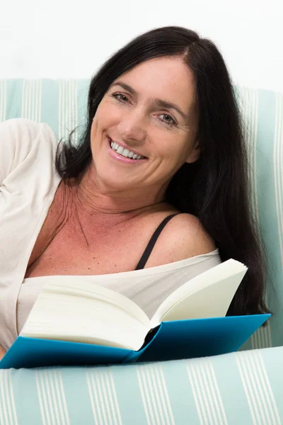 Donna dai capelli scuri sdraiata sul divano e che legge un libro — Foto Stock