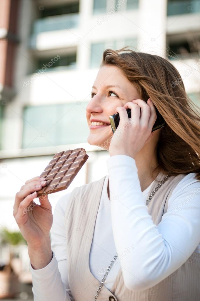 Young woman eating chocolate on the phone