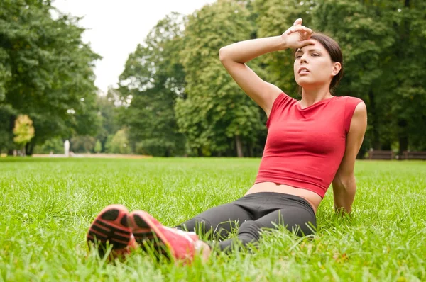 Koppla av i gräs - trött kvinna efter sport — Stockfoto