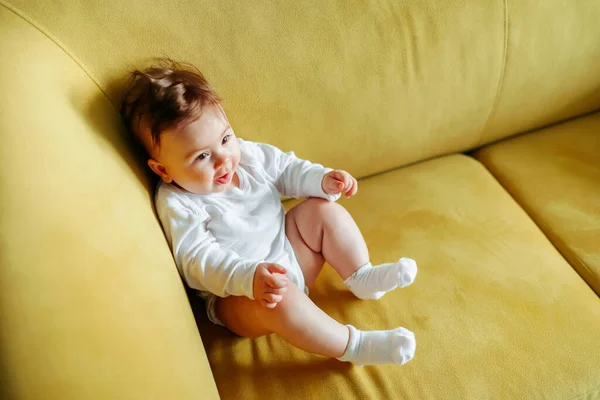 Bambino è seduto sul divano giallo a casa. — Foto Stock