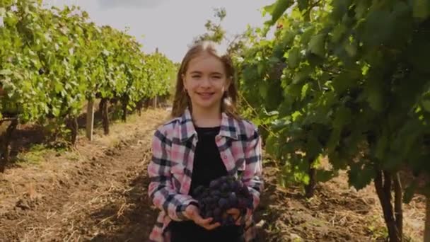 Linda niña con una uva roja en la mano, mirando a la cámara. — Vídeo de stock