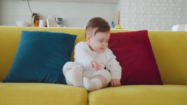 Schattig baby zitten op kleurrijke bank in de woonkamer. — Stockvideo