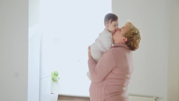 Starsza kobieta trzyma dziecko wnuczka pocałunek w domu młodzi i starzy ludzie razem. — Wideo stockowe