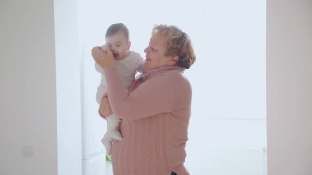 Starsza kobieta trzyma dziecko wnuczka pocałunek w domu młodzi i starzy ludzie razem. — Wideo stockowe