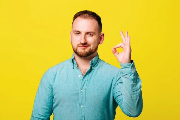 En man tittar på kameran och visar OK gest i teckenspråk på gul bakgrund — Stockfoto