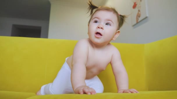 El retrato de la niña jugando en el sofá amarillo en casa en la sala de estar. — Vídeos de Stock