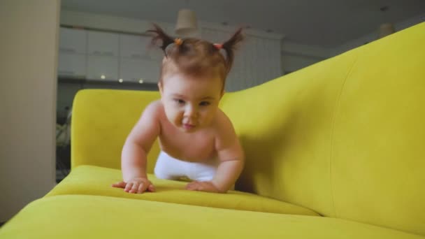 Linda niña en el sofá amarillo dando los primeros pasos en casa — Vídeos de Stock