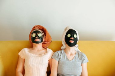 Gözlerinde kozmetik maskeler ve salatalık dilimleri olan iki genç kadın..