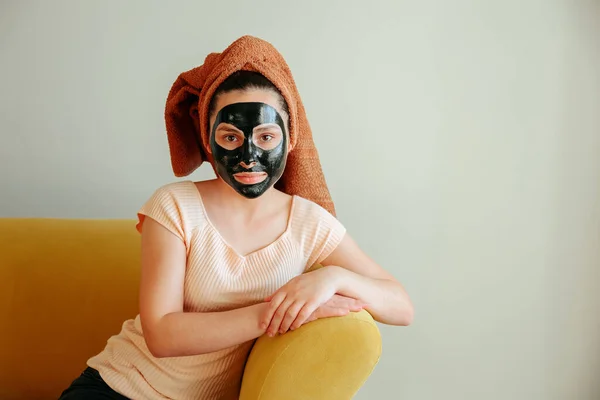 얼굴에 화장품 마스크를 쓰고 머리에 수건을 쓴 젊은 여자의 모습. — 스톡 사진