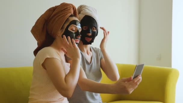 Две девушки с полотенцем на голове и черной маской по уходу за кожей. — стоковое видео