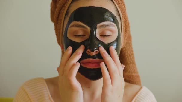 Κορίτσι με μαύρη μάσκα καλλυντικών κοιτάζοντας κάμερα αγγίζει τη μάσκα της με το χέρι της — Αρχείο Βίντεο