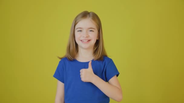 Милая маленькая девочка жестикулирует большими пальцами вверх и смотрит в камеру улыбаясь в камеру — стоковое видео