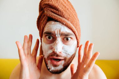 Bağırıyor, korkmuş ve dağınık bir adam güzellik maskesi takıyor kameraya bakıyor.