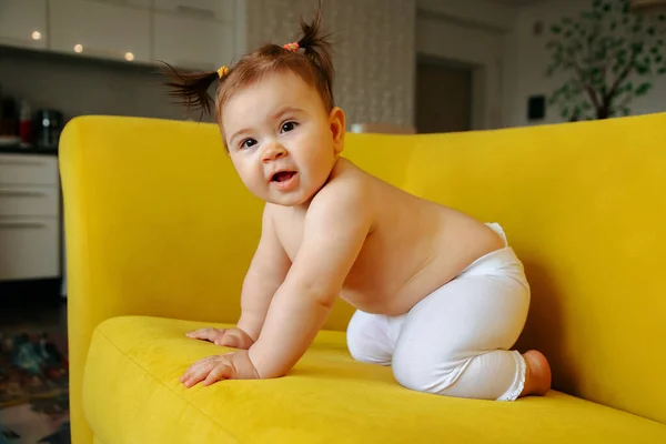 Милая маленькая девочка на жёлтом диване делает первые шаги дома — стоковое фото