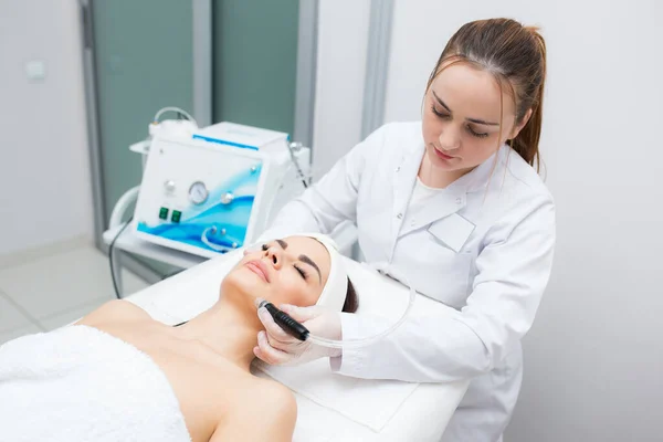 Lovely female doing radiofrequency procedures on her face by a cosmetologist in a wellness center. — Stock Photo, Image