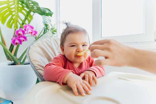 Niedliches kleines Baby wird am Tisch mit einem Löffel gefüttert, — Stockfoto