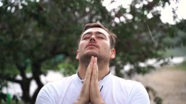 Genç adam dua ediyor, yağmurda dışarıda., 