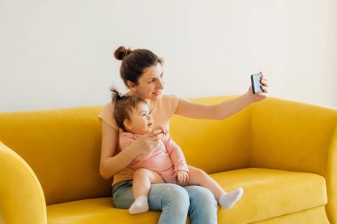 Genç mutlu anne ve bebek akıllı telefon kullanarak babalarıyla görüntülü sohbet ediyorlar..