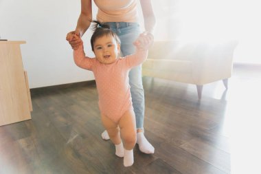 Gülümseyen tatlı bir kız bebek oturma odasında yürümeyi öğreniyor. İlk Bebek Adımları