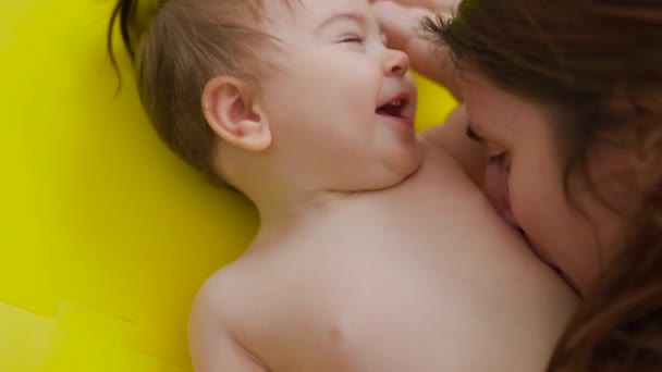 Atractivo bebé alegre y hermoso es besado en el vientre por su madre dulce y encantadora — Vídeos de Stock